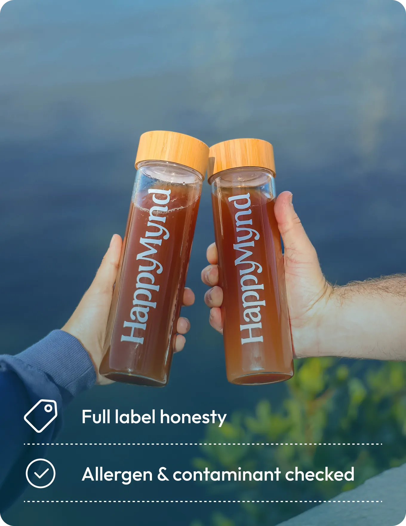 Two hands holding Happy Mund bottles with a scenic background